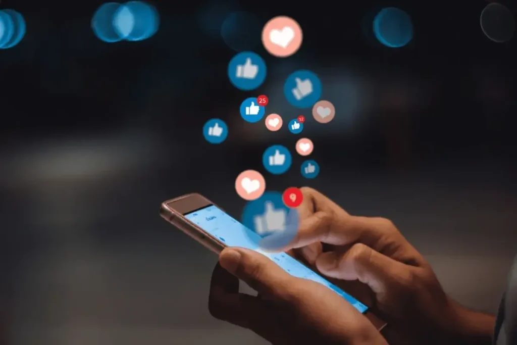 Hand using a smartphone to manage social media engagement, showing floating like and heart icons for digital marketing.