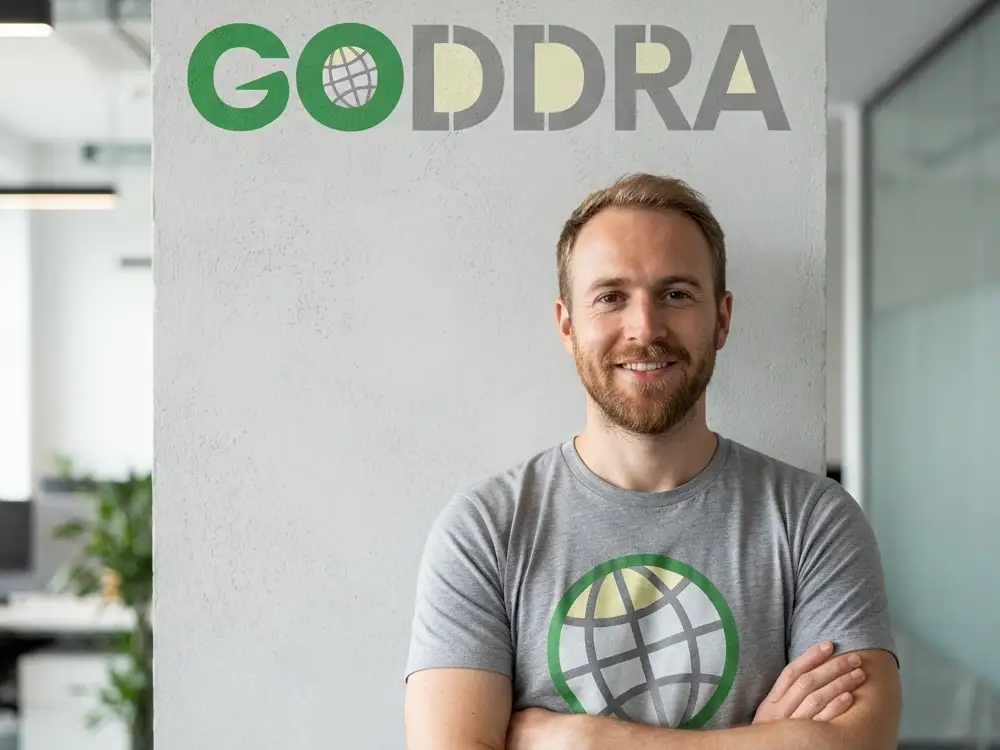 GODDRA agent standing with arms folded under the GODDRA logo in head office.
