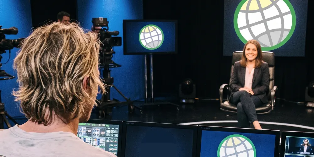 A female applicant sitting in an armchair during a pitch interview, speaking candidly while a GODDRA executive sits across from her with his back turned toward the camera listening intently.